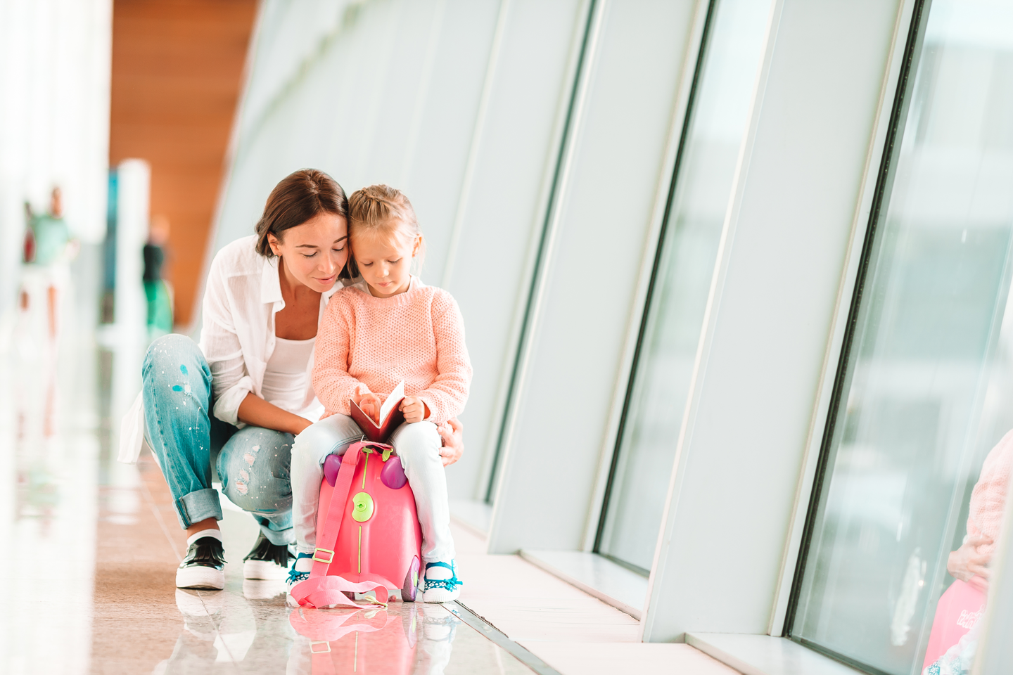 Mother and daughter in airport with pink bag looking at passport